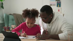 Young father, daughter doing homework and sitting at table in apartment room spbd. Closeup view of American African girl looks into notebook and reads, man helps her and sits at desk with tablet at - Powered by Shutterstock - Get 15% off with code: PIKWIZARD15