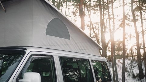 Close shot of camping van with pop up roof at the sunset in the woods in winter . Motorhome parked in a perfect camping spot in rays of sun. High quality 4k footage