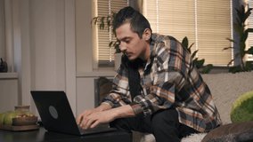Male freelancer in a plaid shirt works at home at a laptop, cozy atmosphere