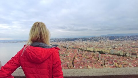 Woman looking Nice French city skyline on des Anglais promenade. Aerial view of cityscape of NICE with Ponchettes beach from panoramic terrace of Colline du Chateau park in Provence of France