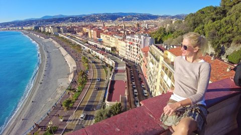 Smiling girl looking French city skyline of Nice on des Anglais promenade. Cityscape of Nice with Ponchettes beach from panoramic terrace of Colline du Chateau park in Blue Coast Provence of France.