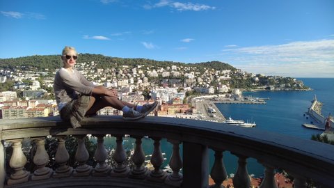 Woman sitting on top view of the Nice city panorama on Port Lympia in Blue Coast and Provence of France. Aerial view of cityscape with lighthouse from the panoramic terrace of Colline du Chateau park.