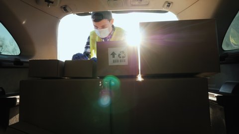 A young man in a medical mask loads boxes of medicines in the trunk of a car
