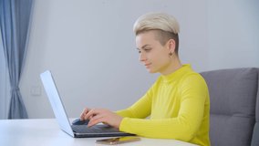 Online work and education concept. Beautiful young woman with short dyed hair typing text on laptop keyboard at home during lockdown. Professional freelancer female working online with modern notebook