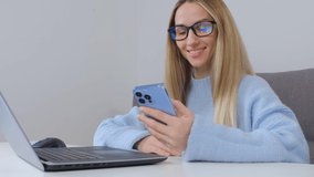 Excited young woman browsing internet news feed in mobile phone. Happy white blonde female using modern smartphone for entertainment and communication. Freelancer female networking online