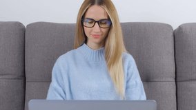 Happy freelancer woman typing on laptop computer. Young white blonde female in glasses working on modern notebook pc at home. Freelance writer person doing distant work online during lockdown