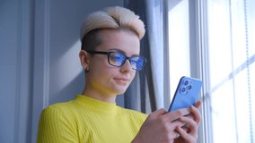 White woman with short dyed hair typing message online in social media app on modern smartphone with triple camera. Young adult female with tomboy style haircut using mobile phone for communication