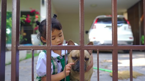 Cute Asian Little girl hugging French bulldog at metal fence during pandemic.