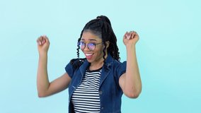 Cute cheerful young African American girl in blue clothes poses and dances in a photo studio. Teen girl standing on a solid light blue background