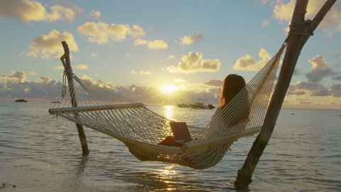 A young woman entrepreneur uses a laptop to work on the hammock at ocean. A businesswoman who works professionally to plan the work, she smiles and congratulates her business is doing well.