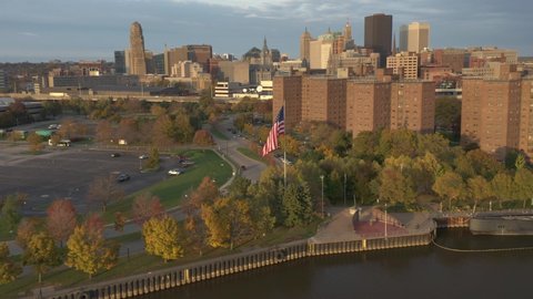 American flag waving against Buffalo NY urban skyline, aerial flyby with zoom