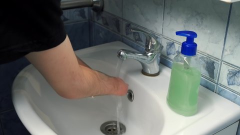 Man with amputated two hands is washing his hands at home in bathroom in sink, closeup view. Everyday routine life of guy person with disabilities. Person with a physical disability.