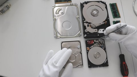Opened hard disk drive. Technician repairing hard drive in service center workshop, hands close up.