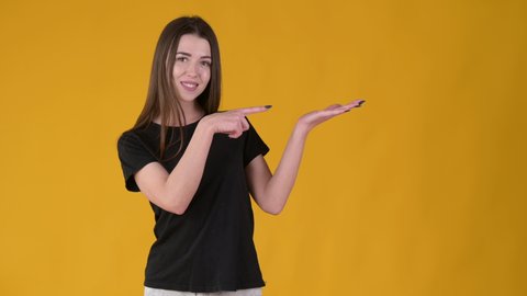Young Happy girl with long hair in a black T-shirt pointing empty place on her palm and smiling at the camera. Attractive woman showing empty space for commercial image. People lifestyle