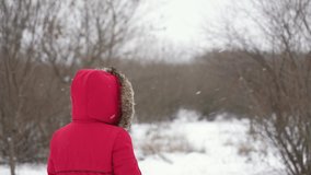 Rear view 4k slow motion stock video of anonymous woman admiring snowy winter weather. Person raises hand in red glove to catch falling snowflakes on palm. Happy winter time, Christmas weather concept