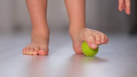Little boy massaging with ball his foot. Exercise stimulates right development of foot. Flat feet correction exercise. close up Shot video. Slow motion