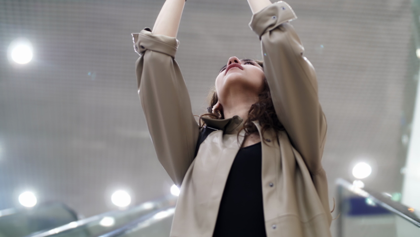 A girl takes pictures of herself on a escalator in a shopping mall. Photo on smartphone. Blurred store lights.