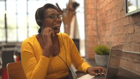 African woman in headset, smiling at camera working in customer service as call center operator, providing consultations on phone. African American business woman taking a sales call using a laptop.