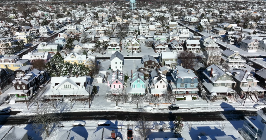 Aerial of small town America covered in winter snow. Painted Victorian homes in quiet daytime snowy scene.