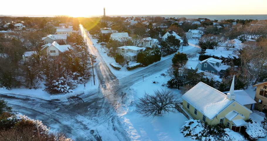 Cape May Point New Jersey. Homes and yellow church, lighthouse at bright sunrise. Aerial orbit of freshly plowed streets.