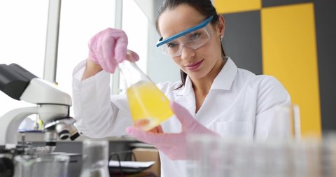 Woman scientist chemist shaking yellow liquid in flask in laboratory 4k movie