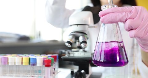 Scientist in flask stirs purple liquid in laboratory closeup