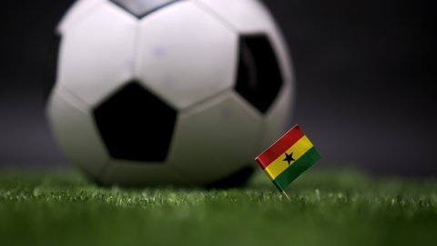 Ghana flag on the football field. Soccer championship. Football classic black and white ball rolls in the background. Sports Competition. The national flag of the country. Green fresh lawn grass
