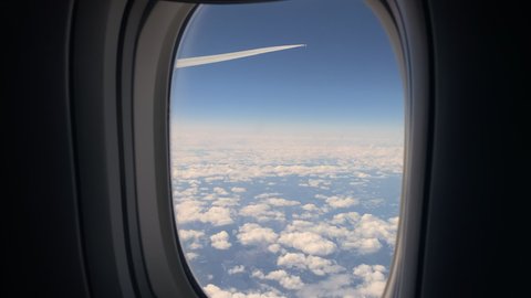 Aircraft porthole. Airplane flight, window view. Wing, blue sky and white clouds. Commercial airlines. Air travel. Tranquility, peace nature. Tourist flying to destination.