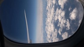 Vertical video. Aircraft porthole. Airplane flight, window view. Wing, blue sky and white clouds. Commercial airlines. Air travel. Tranquility, peace nature. Tourist flying to destination.