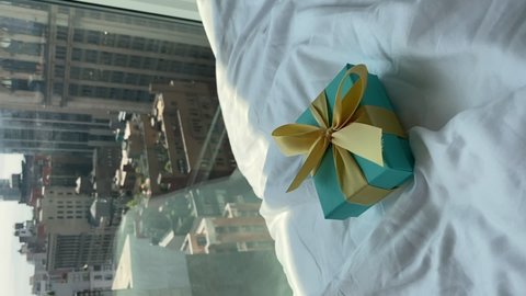 NEW YORK, USA - MAY, 18, 2021: Vertical video. Young woman opens Tiffany blue gift box tied with yellow ribbon. Jewelry ring present for birthday, anniversary, romantic. Panoramic window skyscrapers.