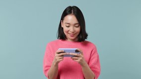 Gambling young woman of Asian ethnicity 20s wears pink shirt using play racing on mobile cell phone hold gadget smartphone for pc games isolated on plain pastel light blue background studio portrait