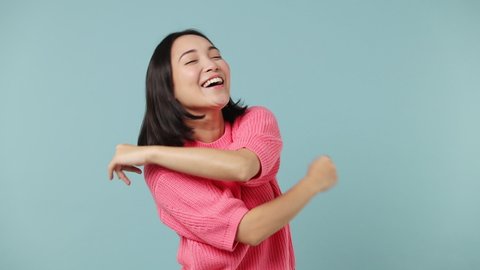 Slow motion vivid fun young woman of Asian ethnicity 20s wears pink shirt dance fool around have fun gesticulating with hands enjoy relax isolated on plain pastel light blue background studio portrait
