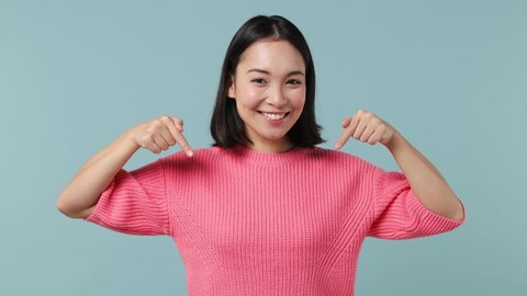Smiling happy young woman of Asian ethnicity 20s years old wears pink shirt pointing fingers down on workspace area copy space mock up isolated on plain pastel light blue background studio portrait