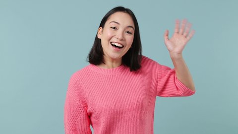 Friendly young woman of Asian ethnicity 20s wears pink shirt look around for friend find waving meet greet with hand as notices someone isolated on plain pastel light blue background studio portrait