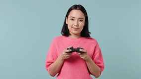 Gambling happy blithesome young woman of Asian ethnicity 20s years old wears pink shirt hold in hand play pc game with joystick console isolated on plain pastel light blue background studio portrait