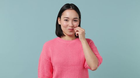 Secret young woman of Asian ethnicity 20s wears pink shirt look aside say be quiet shhh gesture close her mouth lock and throw away key isolated on plain pastel light blue background studio portrait