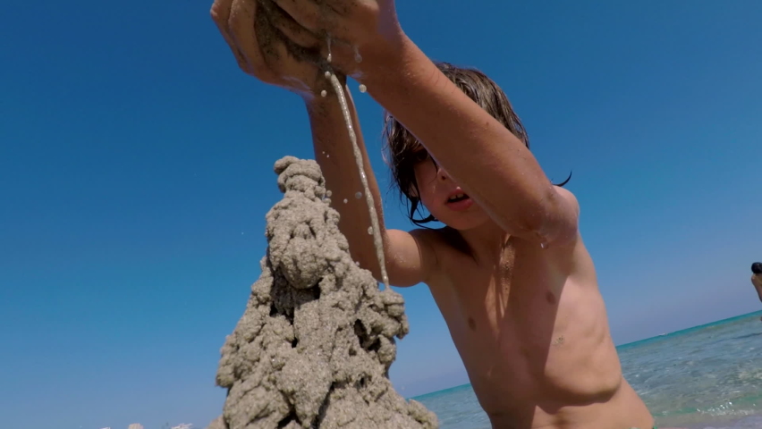 Summer vacation. Close up of child building sand castle on seashore, relaxing near water. Gopro camera shaking. Sand is perfect natural resource for developing kids fine motor skills. Summertime.