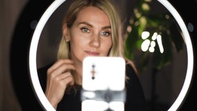 Adorable blonde woman streaming beauty vlog on mobile phone with ring lamp from home Video 4k
