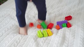 little cute boy of two years old plays children's constructor sitting on the bed Video 4 k
