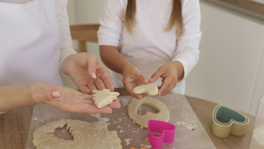 Closeup of caucasian family mother and daughter holding in hands raw heart-shaped and Christmas tree cookies making diverse figures with cookie cutters, mom and kid using biscuit figurines.