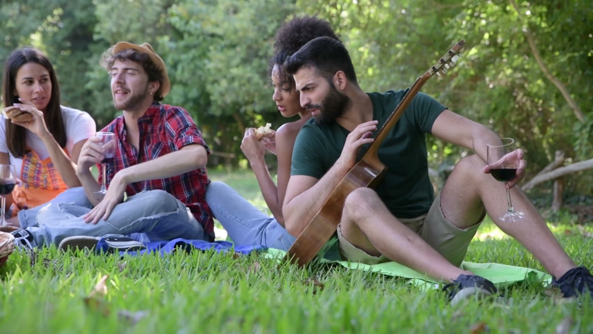 Picnic in the countryside - Group of young friends, at sunset on spring day are sitting on the ground in a park near trees. They drinking red wine and eating grilled meat with barbecue