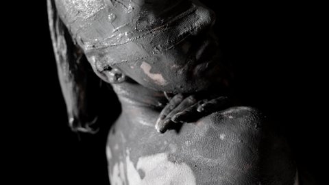 live clay statue of blindfolded woman is moving in darkness, smearing mud on body