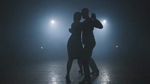 Couple dancing tango in smoky studio with spotlights. Close-up of beautiful couple dancing latin dance. Silhouette in 4K, UHD