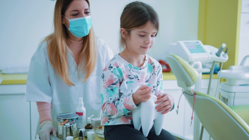 Little girl and the medical staff are playing with 
big healthy tooth model in a dental office.