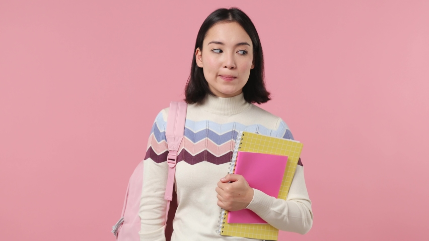 Girl teen student of Asian ethnicity wears shirt backpack hold books say oops ouch oh omg isolated on plain light pink background studio portrait. Education in high school university college concept Royalty-Free Stock Footage #1086335930