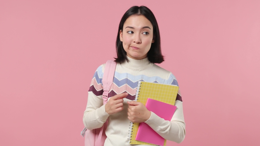 Confused fun girl teen student of Asian ethnicity 20s wears shirt backpack hold books spreading hands say oops ouch oh omg i am so sorry isolated on plain pastel light pink background studio portrait Royalty-Free Stock Footage #1086336014