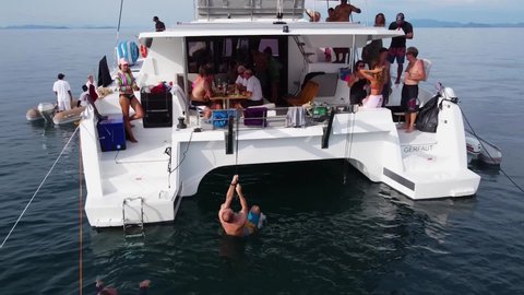 Phuket, Thailand, 20, December, 2019:
A man has fun while swimming, climbing a rope on a sailing catamaran, a lot of people on board during a boat trip