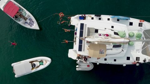 Phuket, Thailand, 23, January, 2022:
Top view of a group of tourists swimming and relaxing during a sea cruise on a sailing catamaran, people swim near the boat, drone view