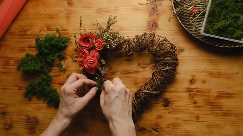 Valentines day decoration, DIY home decor crafts. Female hands decorates heart shaped floral wreath using moss. Florist at work.