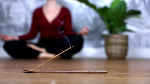 Mindful woman meditating at home with burning incense sticks, siting in lotus pose. Holding hands in lap with palms facing upwards.